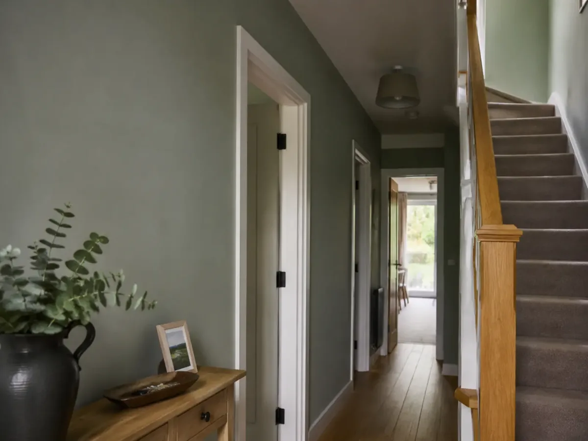 Sage green hallway with clean white door frames and a timber staircase.